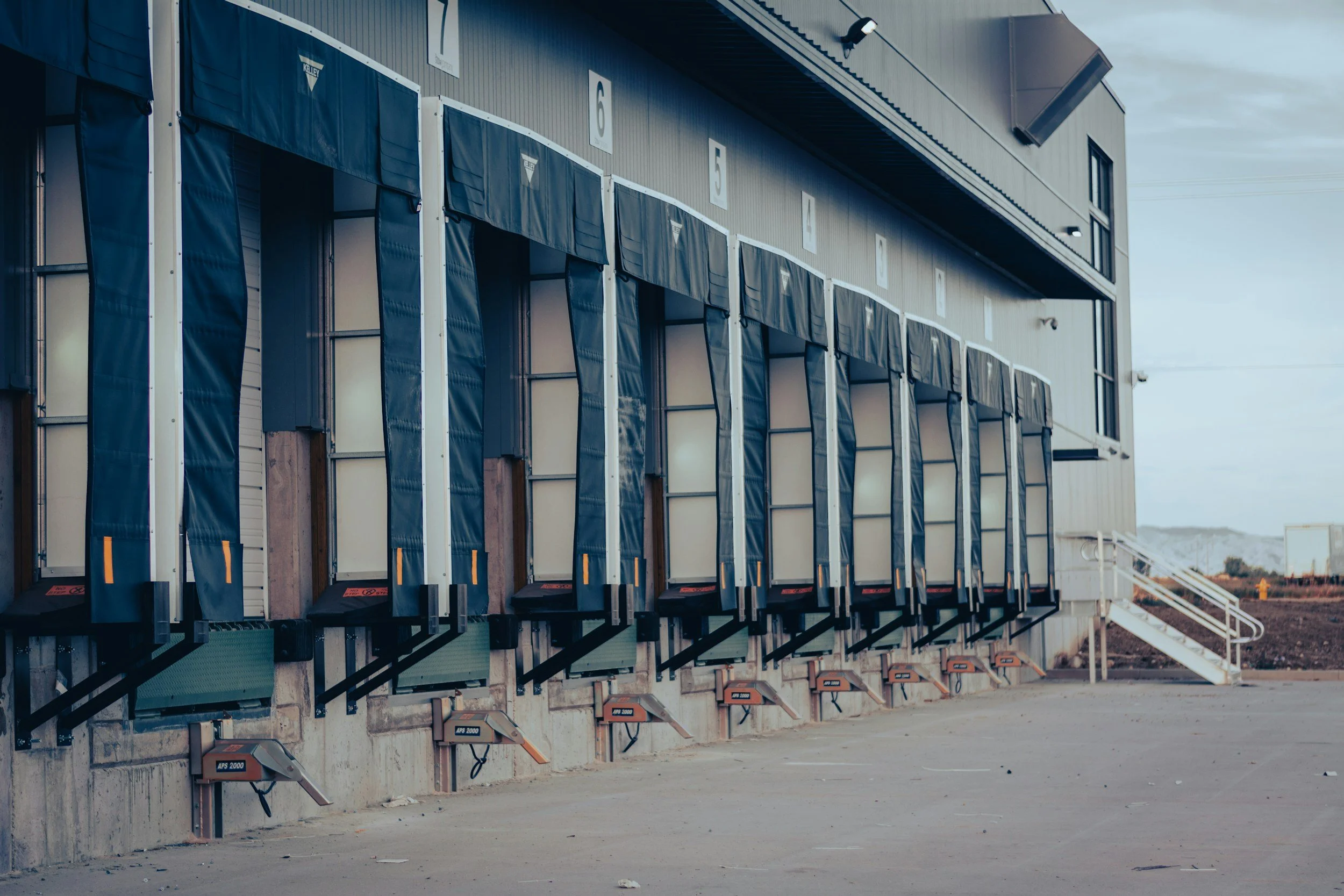 A row of dock doors at a distribution center with loading dock bumpers and stairs leading to the building