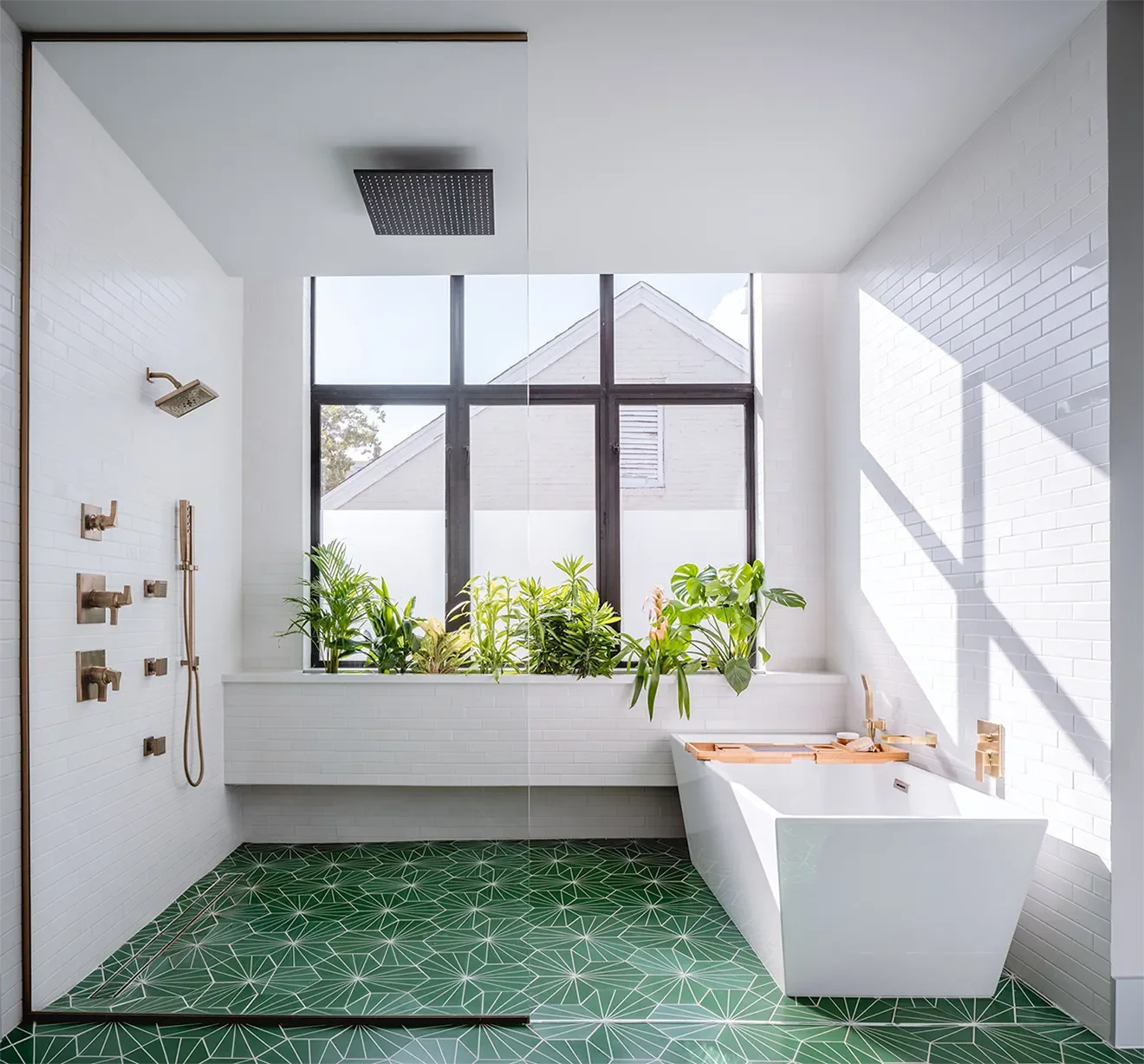 Modern bathroom with white brick walls, large window, green plants, white bathtub with wooden tray, and green geometric patterned floor.