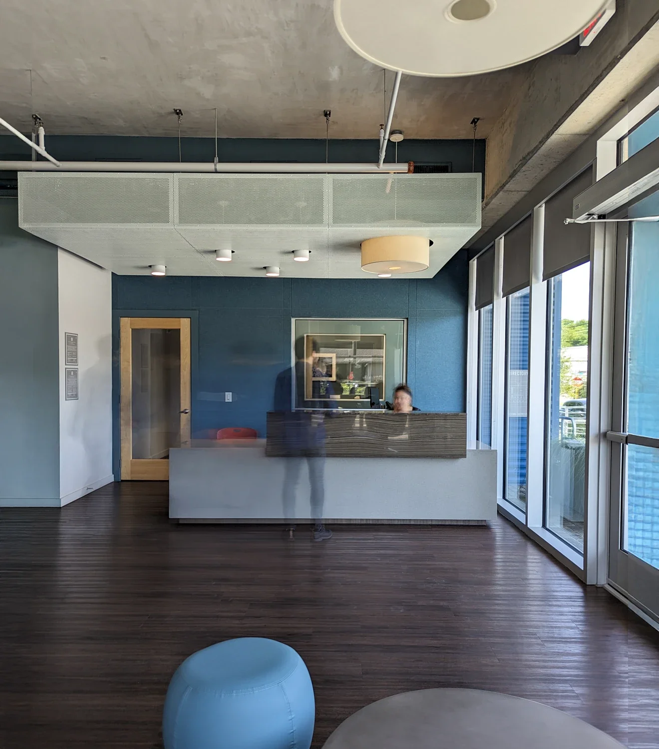 Modern office lobby with a reception desk, a glass windowed exterior, and minimalistic furniture.