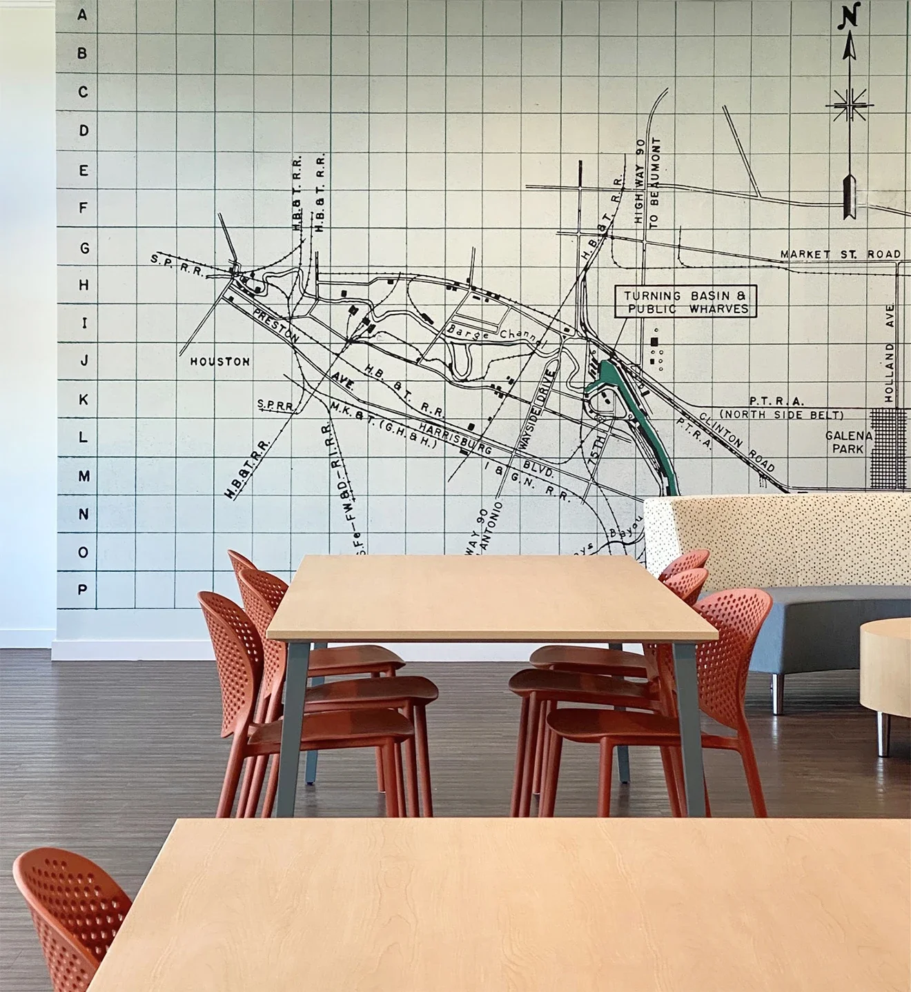 A large wall map of a city's transit system and streets, with a seating area consisting of two tables and red chairs, and a modern sofa in a room with wooden flooring.