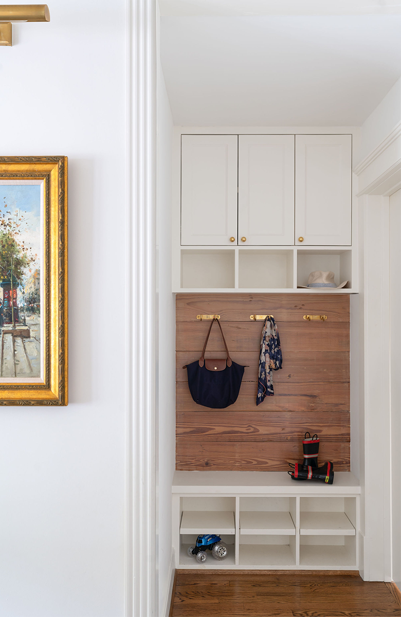 Entryway with built-in white cabinets, a wooden panel with hooks holding bags and scarves, cubbies with a toy truck, and artwork on the adjacent wall.