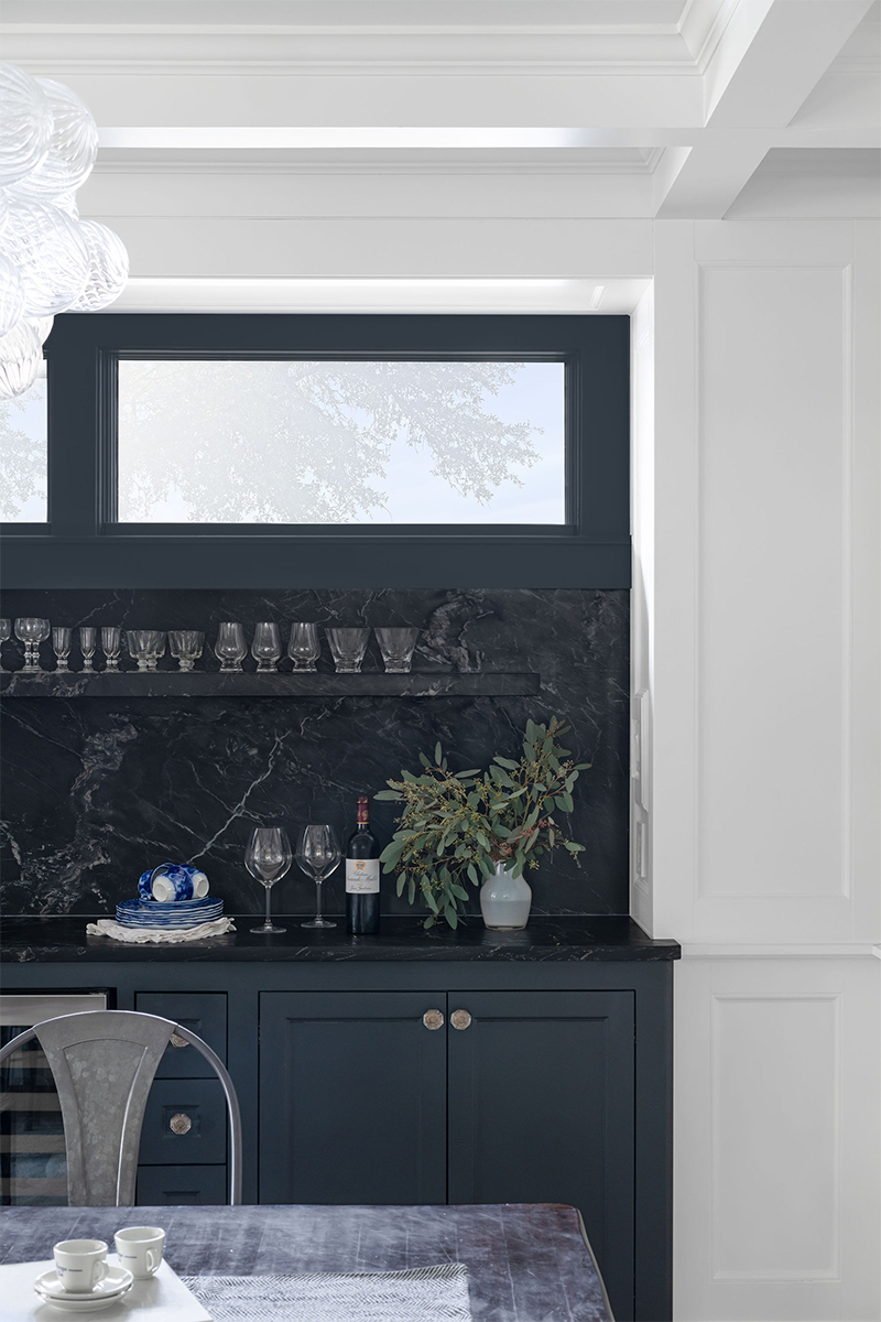 Modern kitchen with dark blue cabinets, black marble backsplash, and a large window with trees outside.