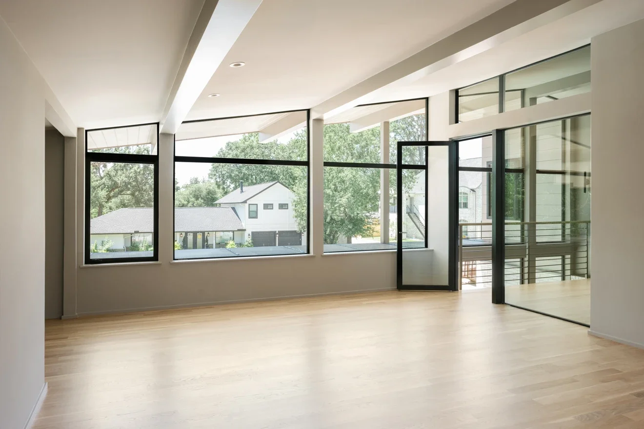 Empty modern room with large floor-to-ceiling windows and glass door, light wood flooring, and street view outside.