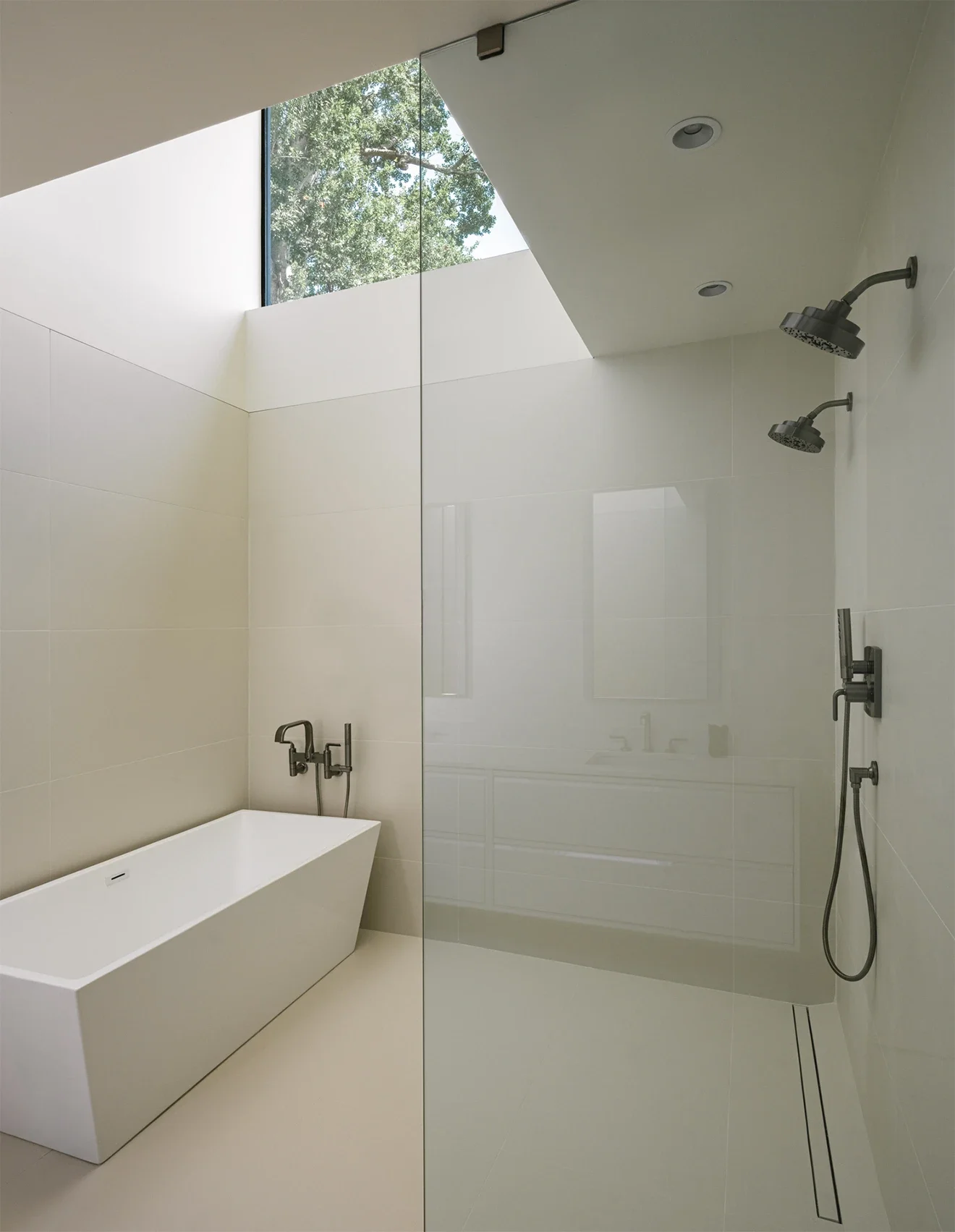 Modern bathroom with a freestanding bathtub, double showerheads, and a large skylight window showing trees outside.