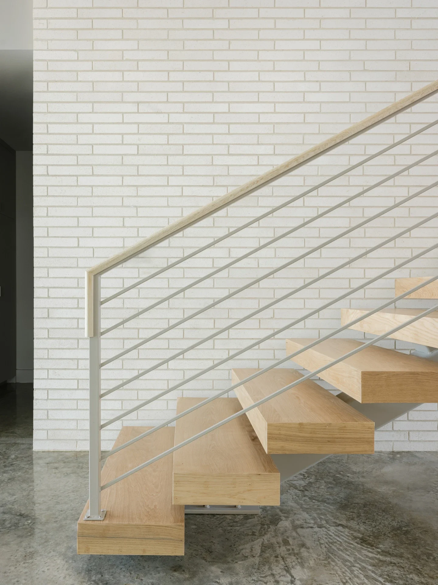Modern staircase with wooden steps and metal railing against a white brick wall.