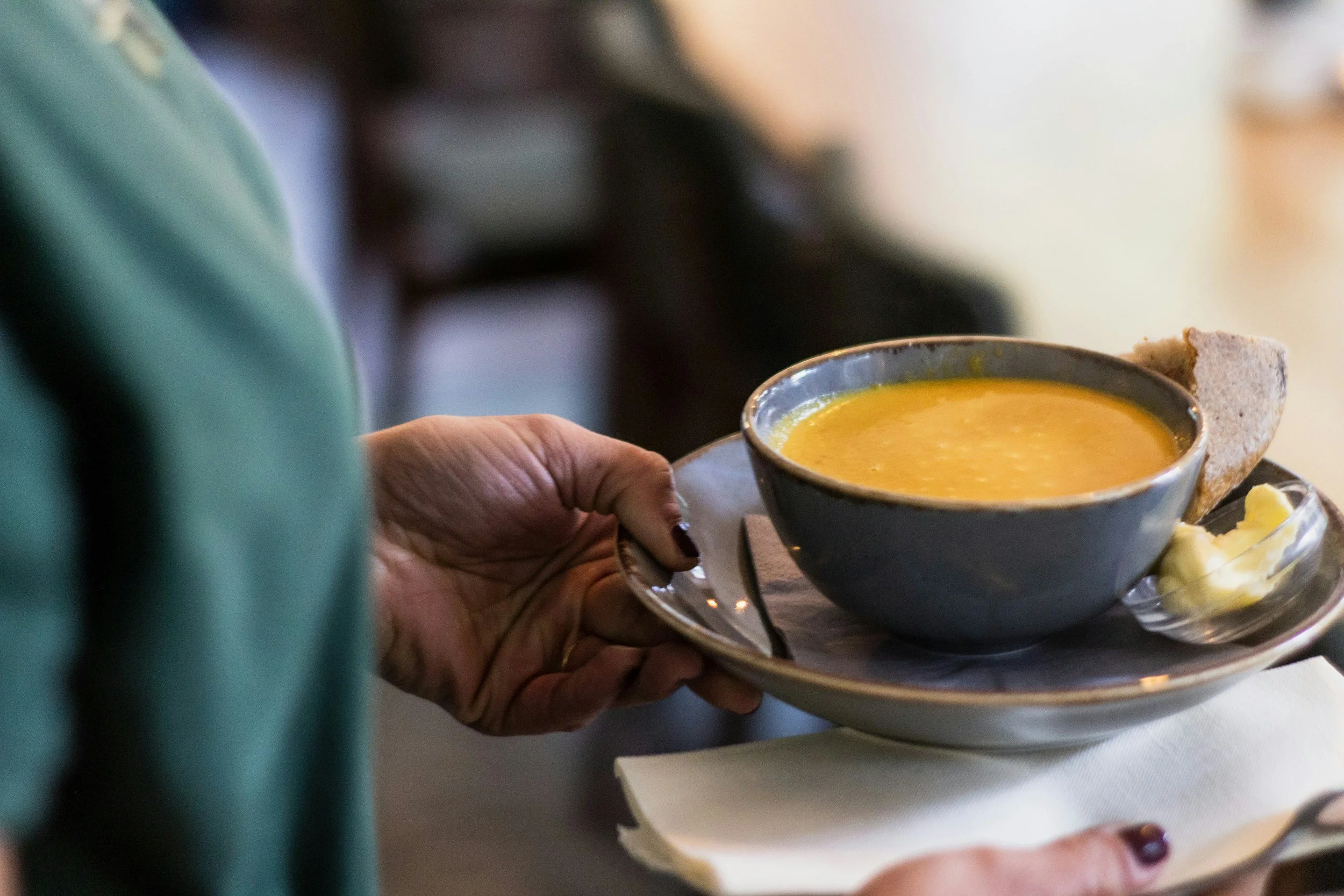 A person holding a delicious looking bowl of vegetable soup with a plate of bread on the side.
