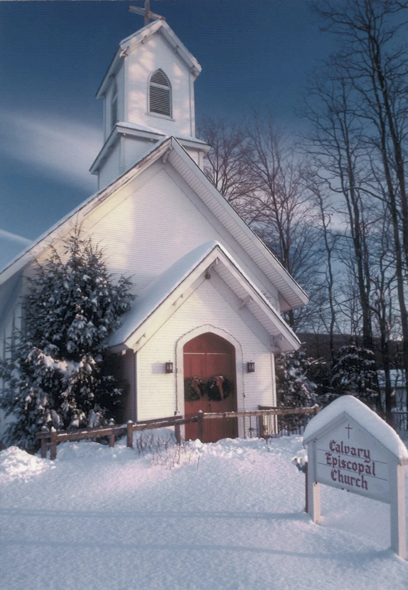 Calvary Episcopal Church and church sign on a winter's day with freshly fallen snow and two wreaths on the red door.