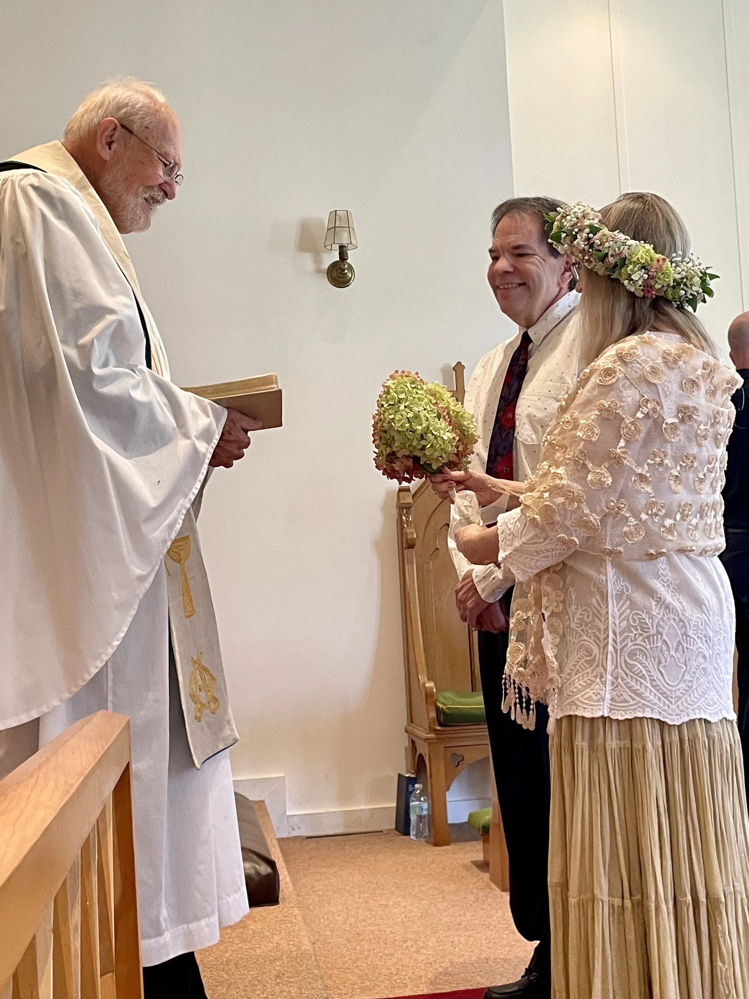 Brown dog with white spots looking up attentively at older male Priest with gray hair who is reading to the congregation.