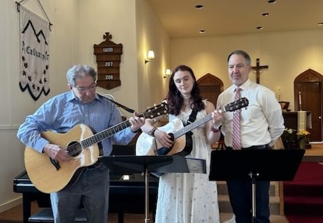 Three musicians playing a hymn at Easter. One man on guitar, another man singing, and a woman playing guitar.