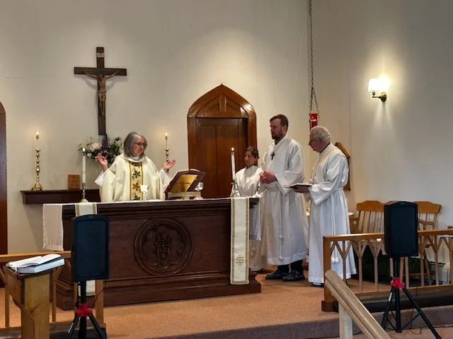 Woman Priest with palms raised during communion. Two female and one male clergy member stand on the right side.