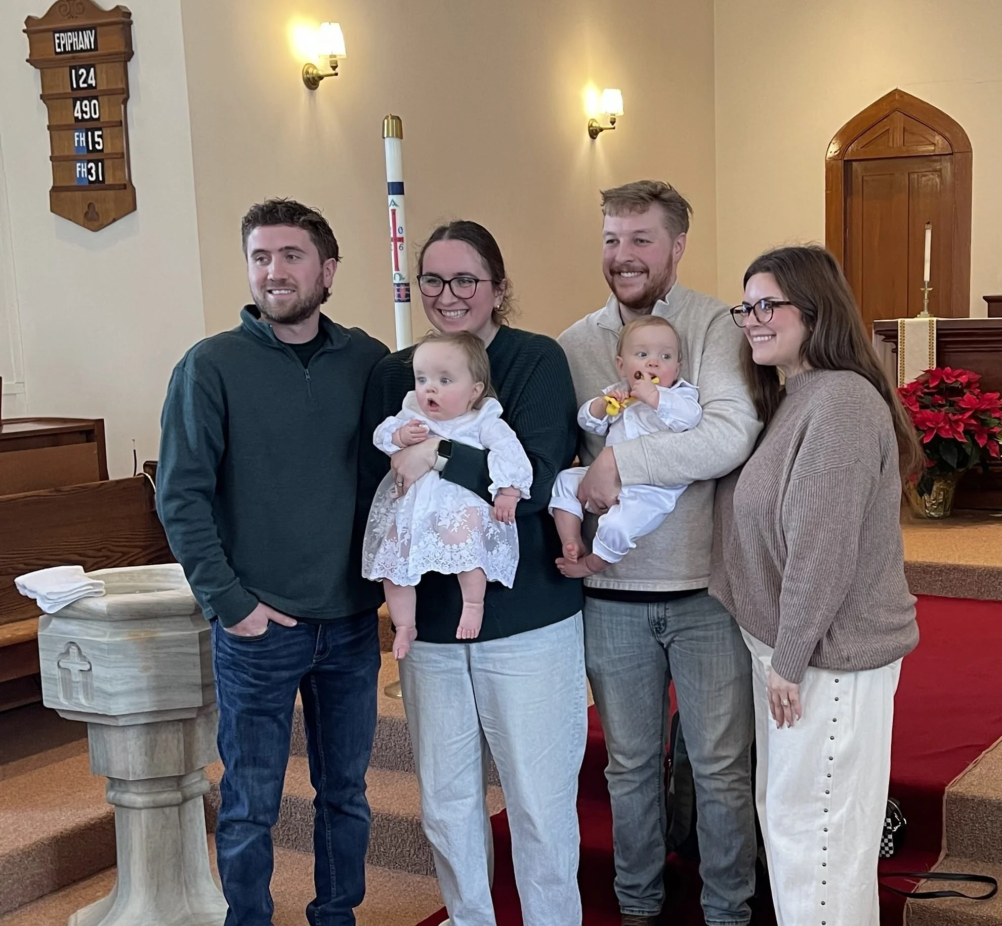 After the baptism ceremony – parents, godparents and twin babies pose for a picture. Their’s a red carpet and red poinsettias.