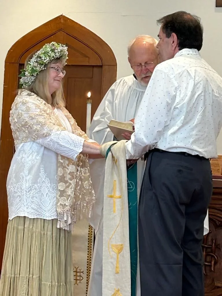 Man and woman holding hands during wedding ceremony with elder male Priest presiding.