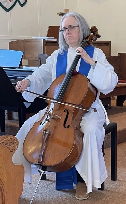 Priest with grey hair in white vestment and blue stole playing cello.