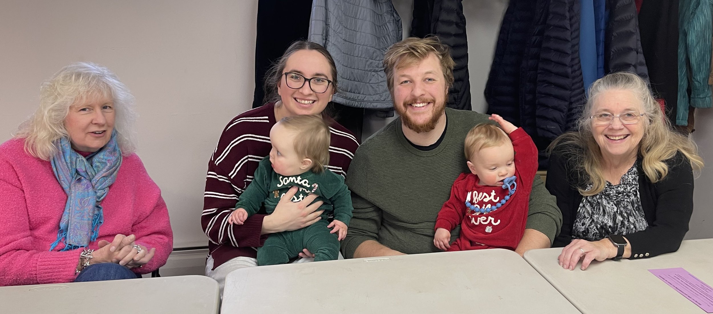 Mother, father, grandmother, woman friend, and two twin babies smile for the camera.