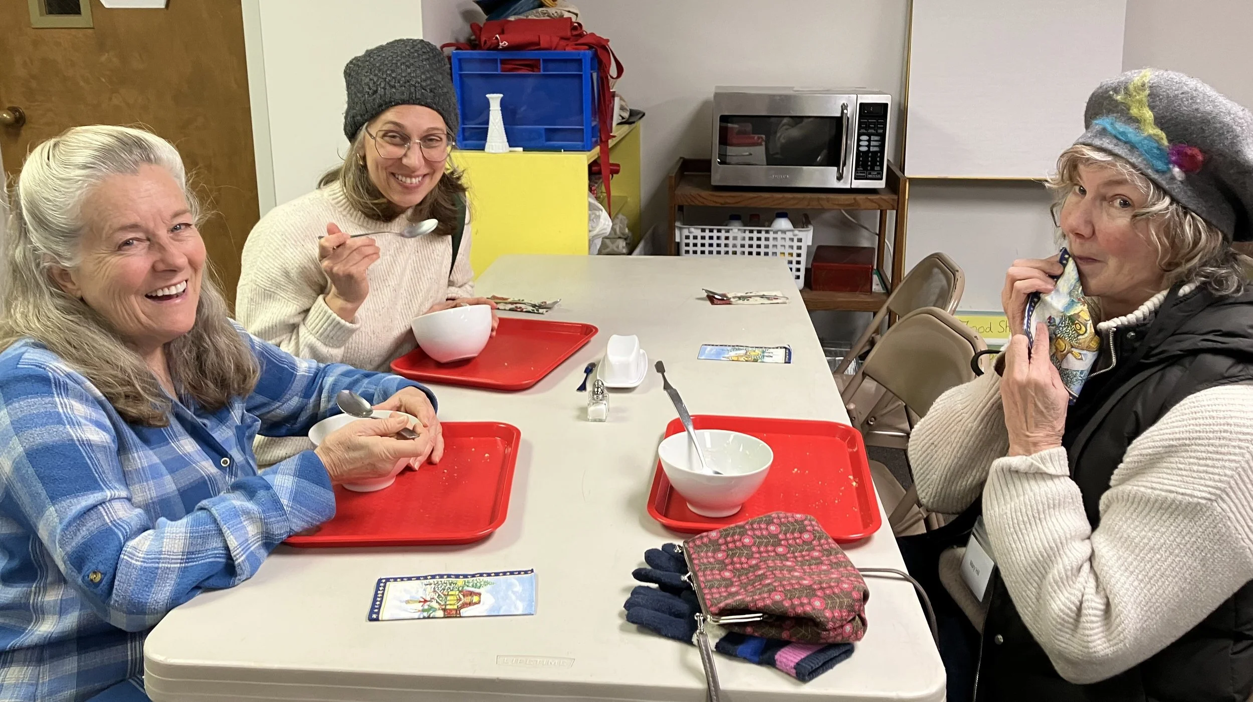 Three women eating soup, one wiping her moth daintily with a napkin.
