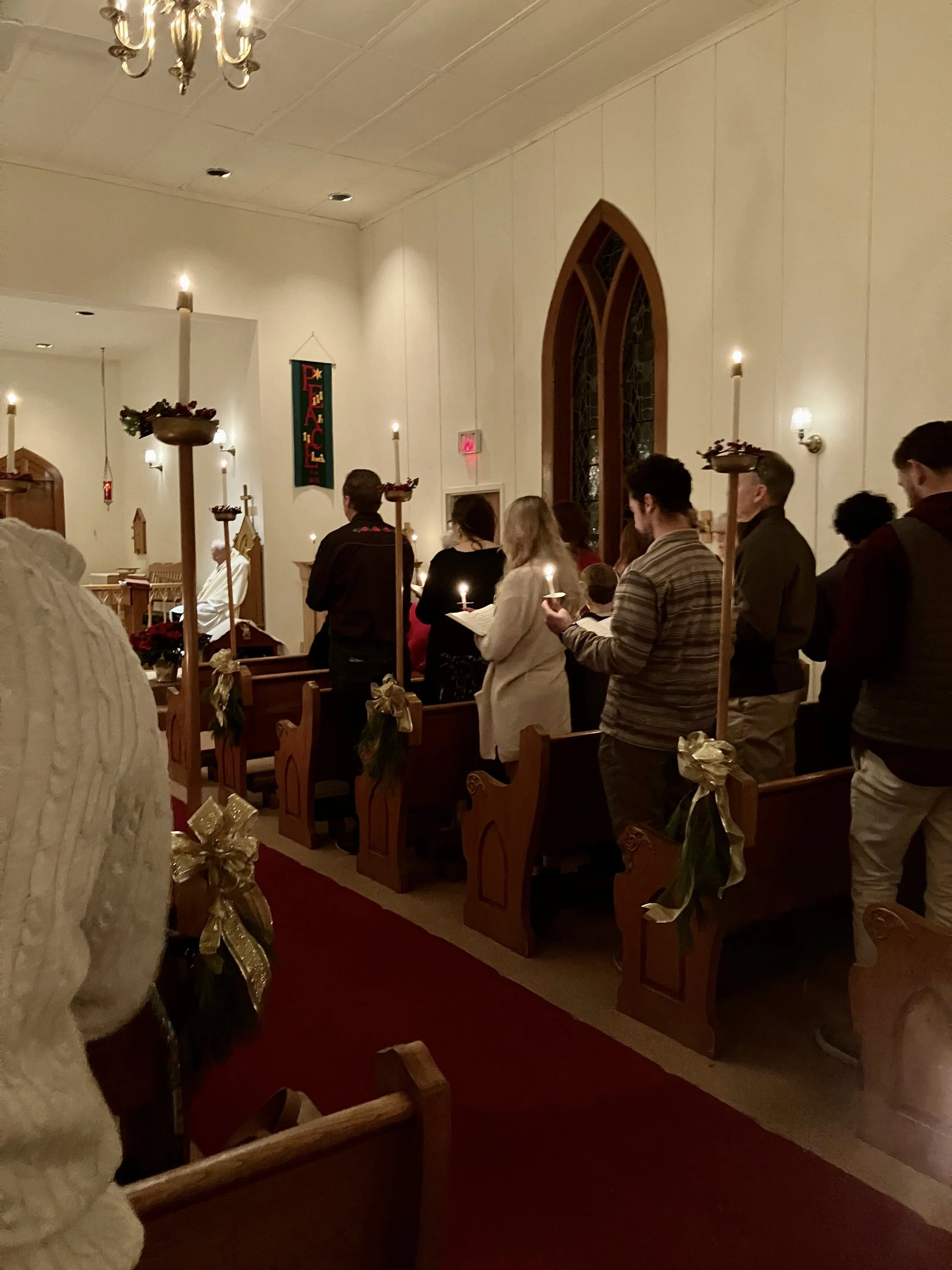 Congregation members standing in pews holding candles during Christmas Eve candlelight service.