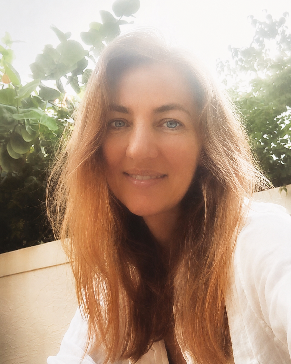 female artist with green blue eyes auburn long hair bright smile in a modern yard seagrapes and plaster wall