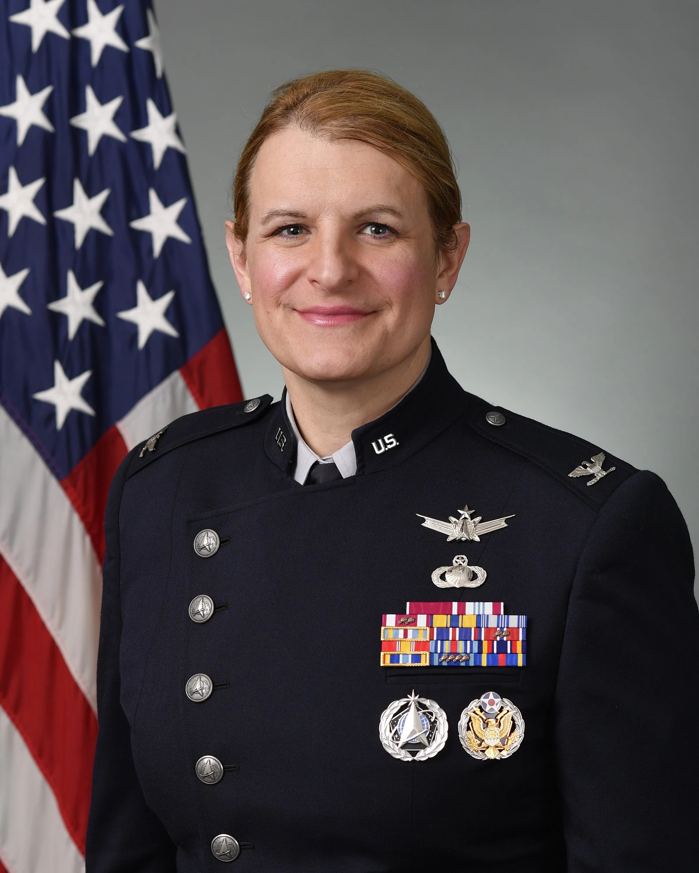 A woman in a U.S. military uniform standing in front of an American flag.