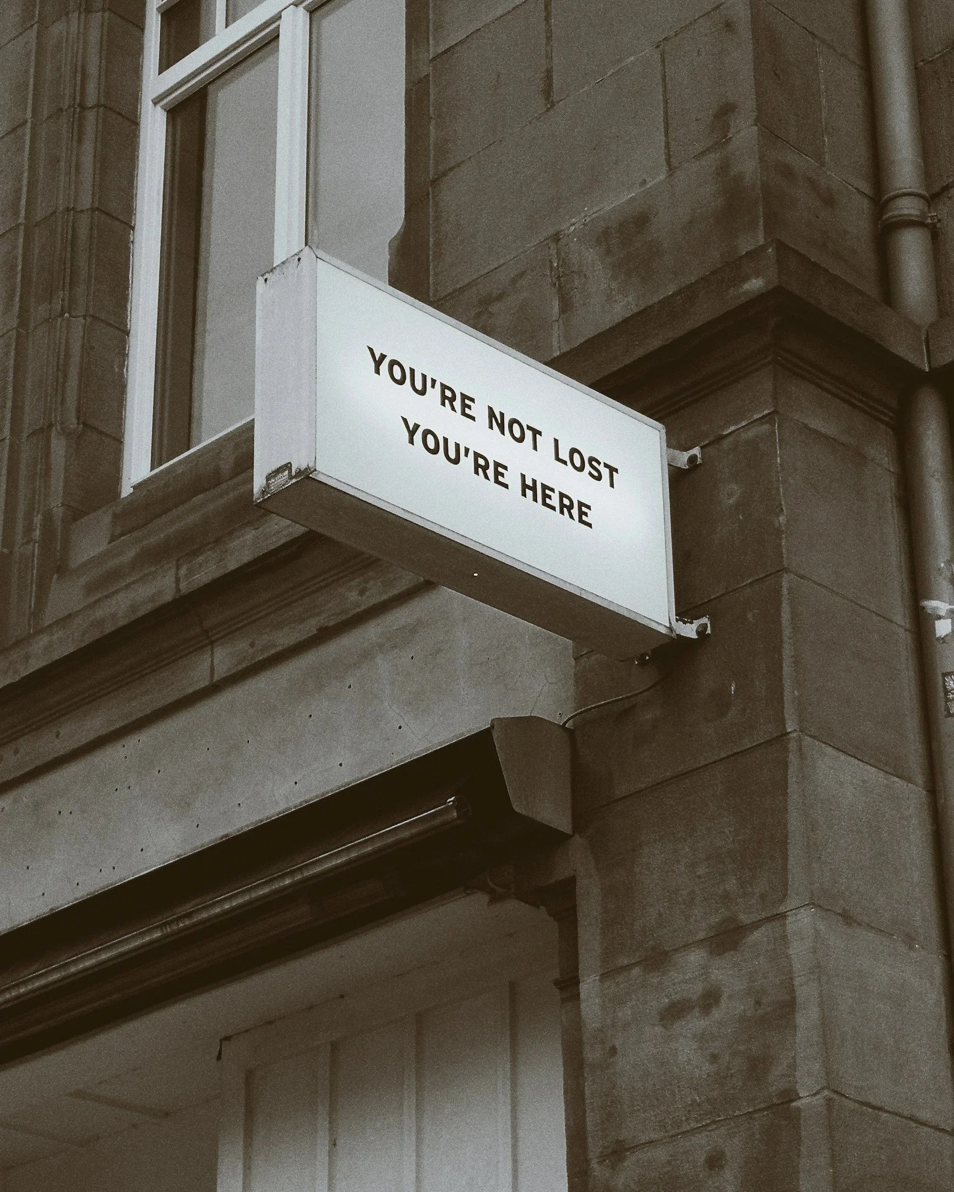 A lit-up sign on the corner of a brick building reads 'You're Not Lost You're Here'.