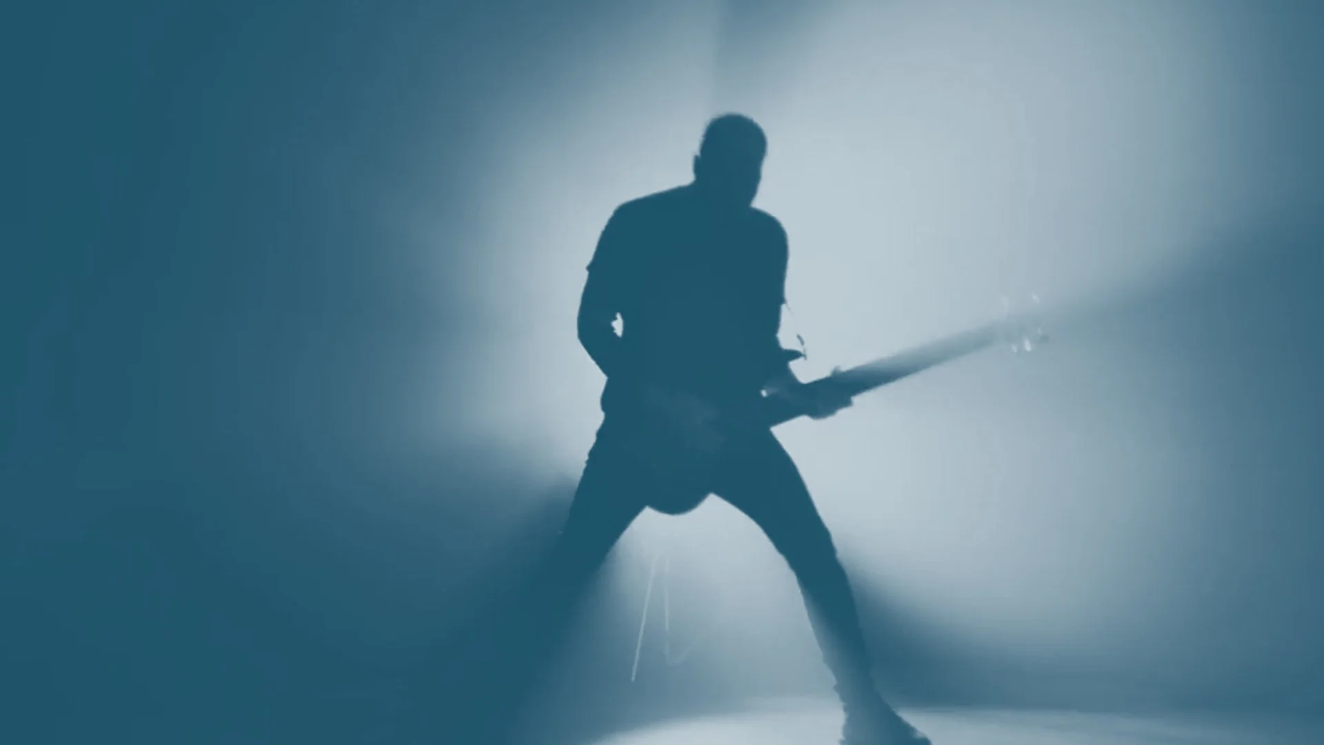 Silhouette of a person playing an electric guitar in a dimly lit setting with a foggy or smoky atmosphere.