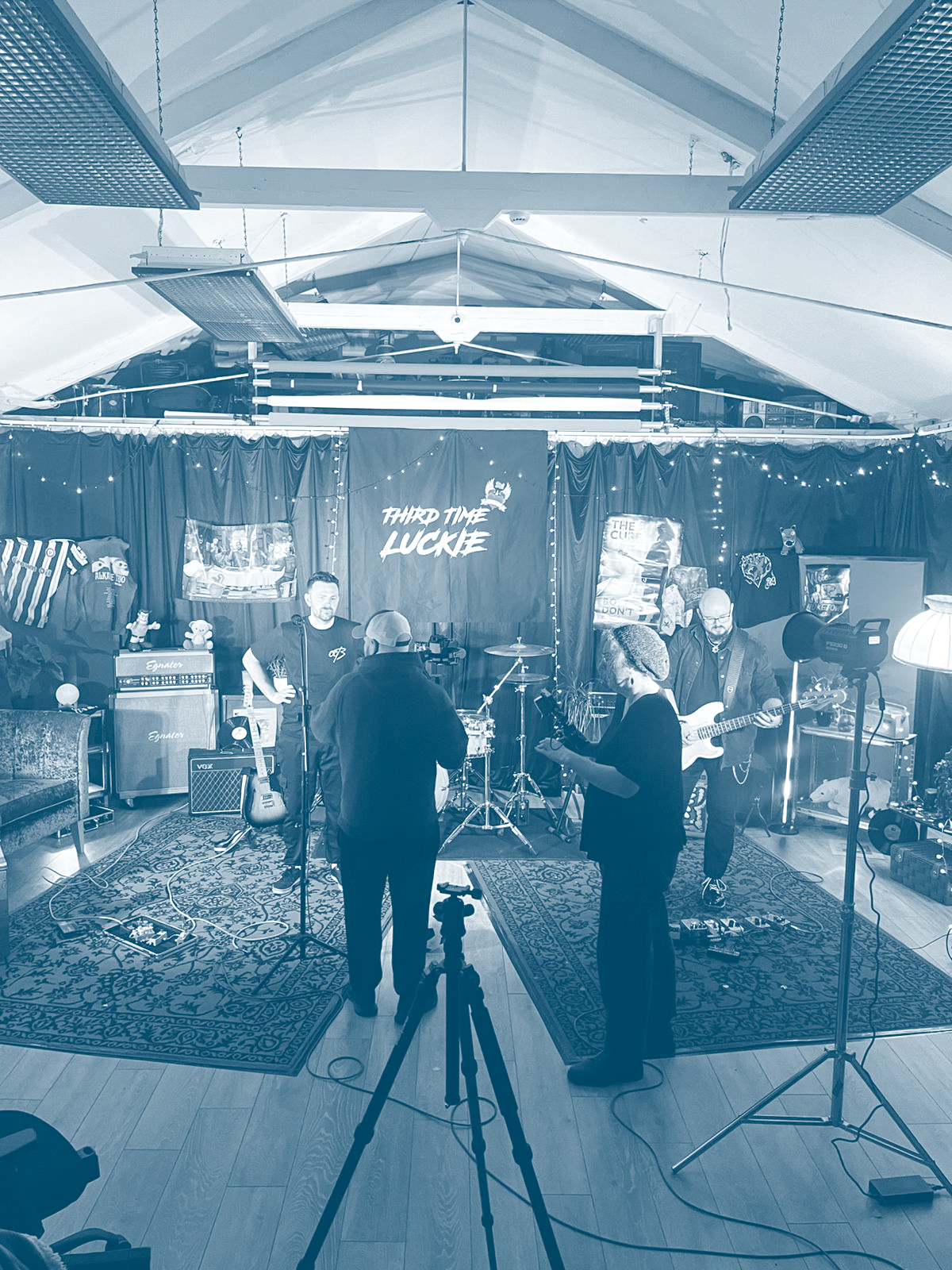 A band named 'Third Time Lucky' performing on stage in an indoor venue with musical equipment and a curtain backdrop.
