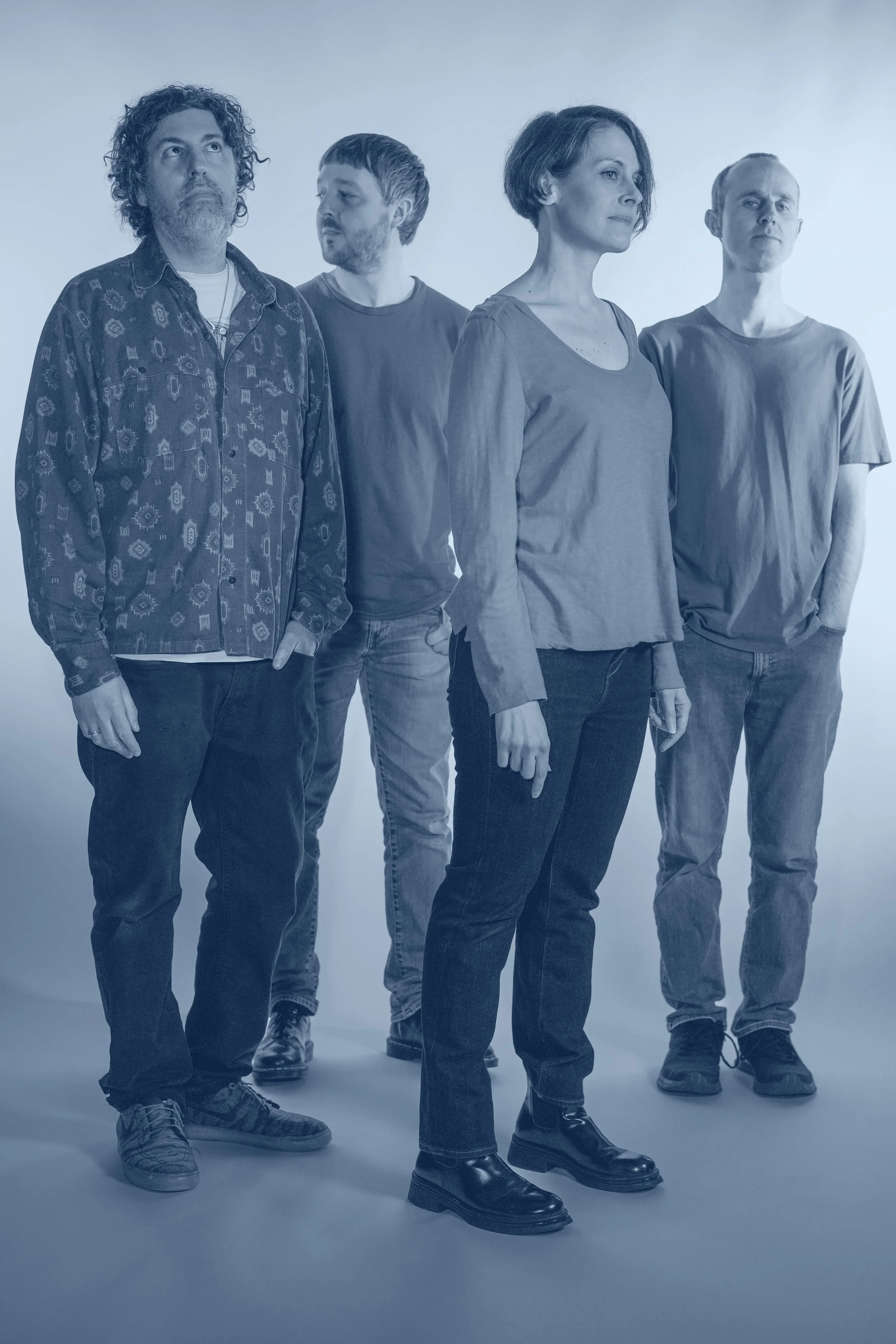 A group of four people standing in a studio with a plain background, looking in different directions.