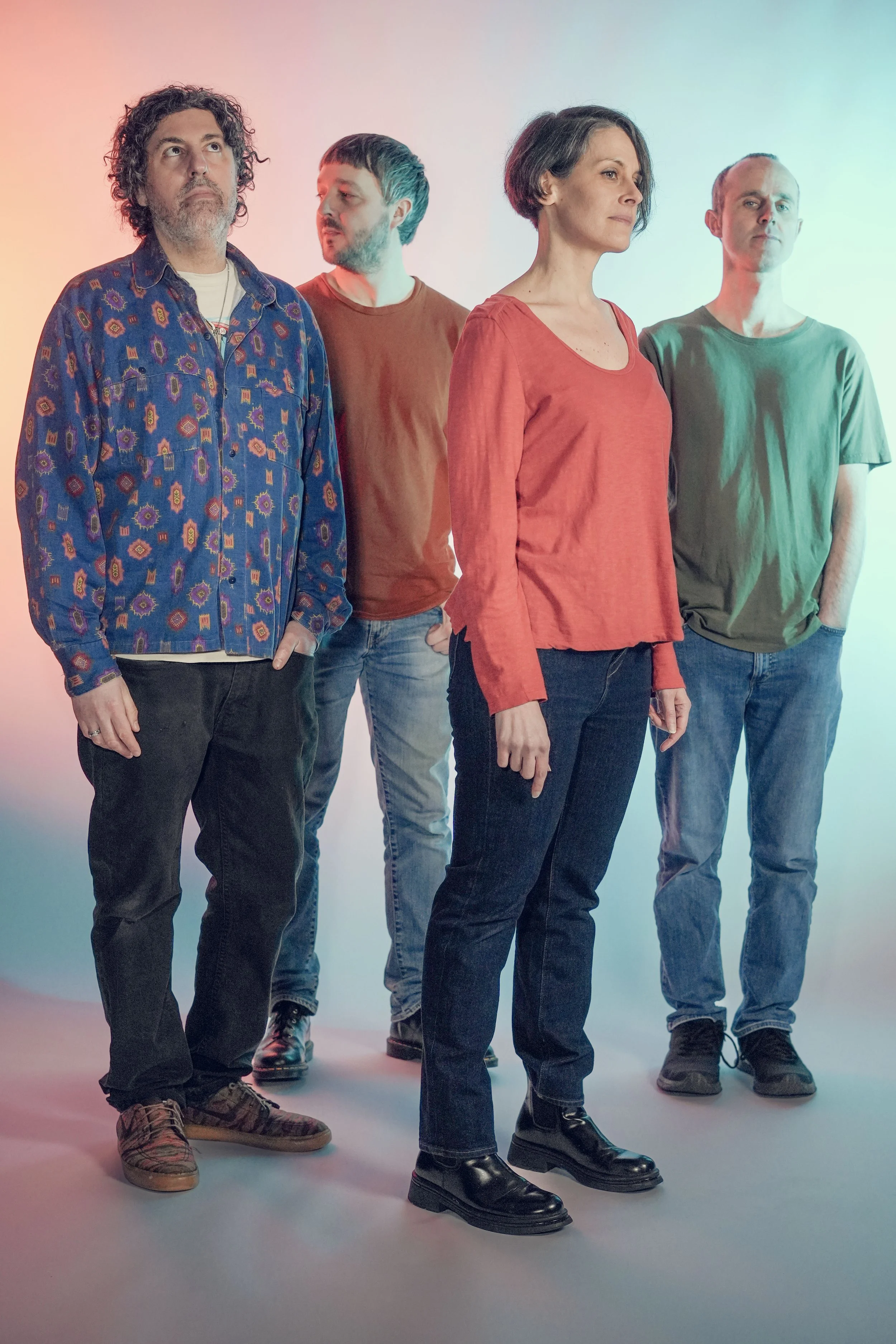 Four people standing in a line against pastel-colored background, looking in different directions.