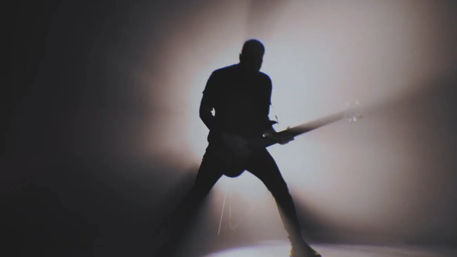 Silhouette of a person playing an electric guitar with a bright light background, creating a contrasted shadow effect.
