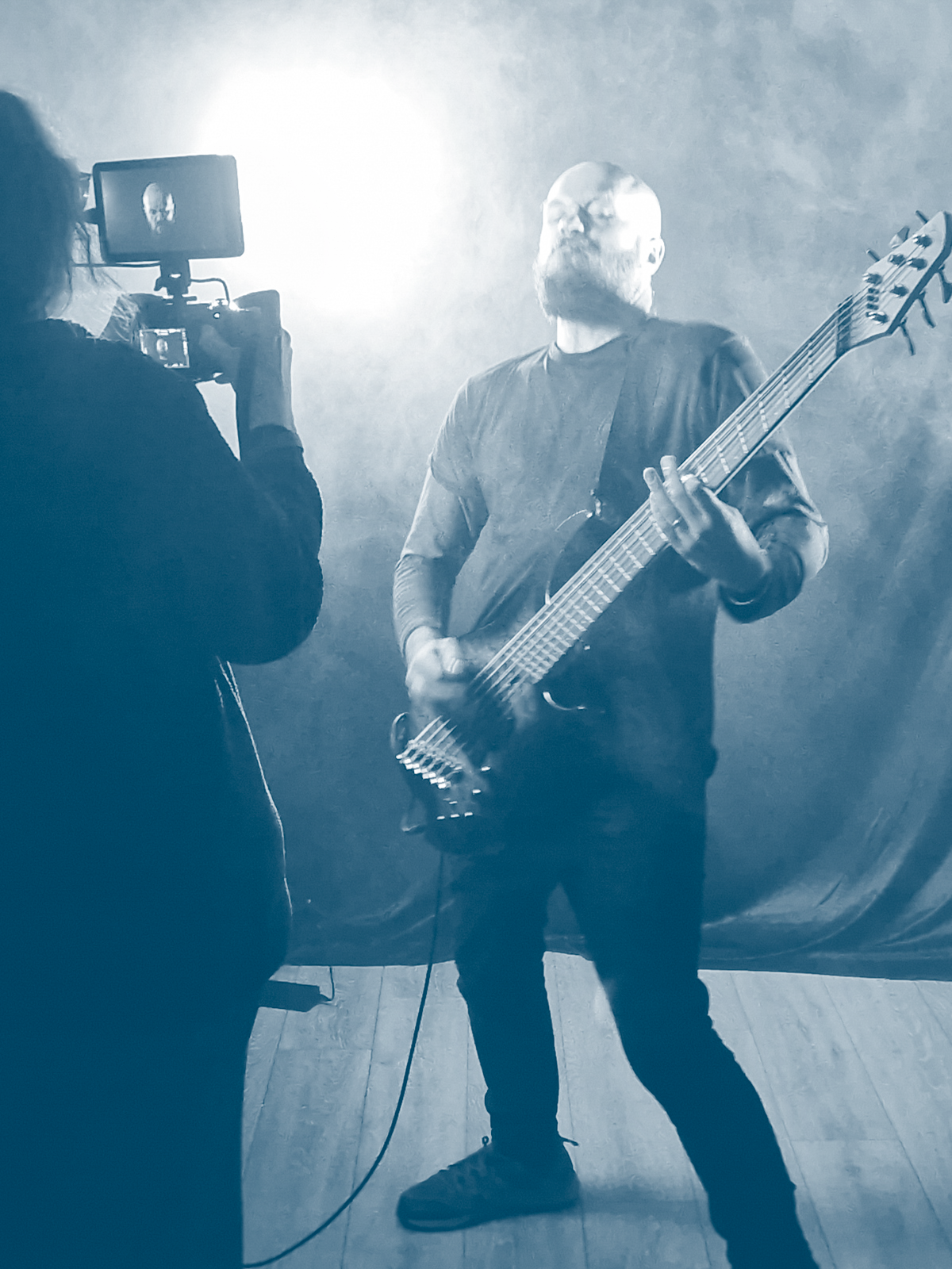 A man playing a bass guitar during a music video shoot with a camera operator filming him.