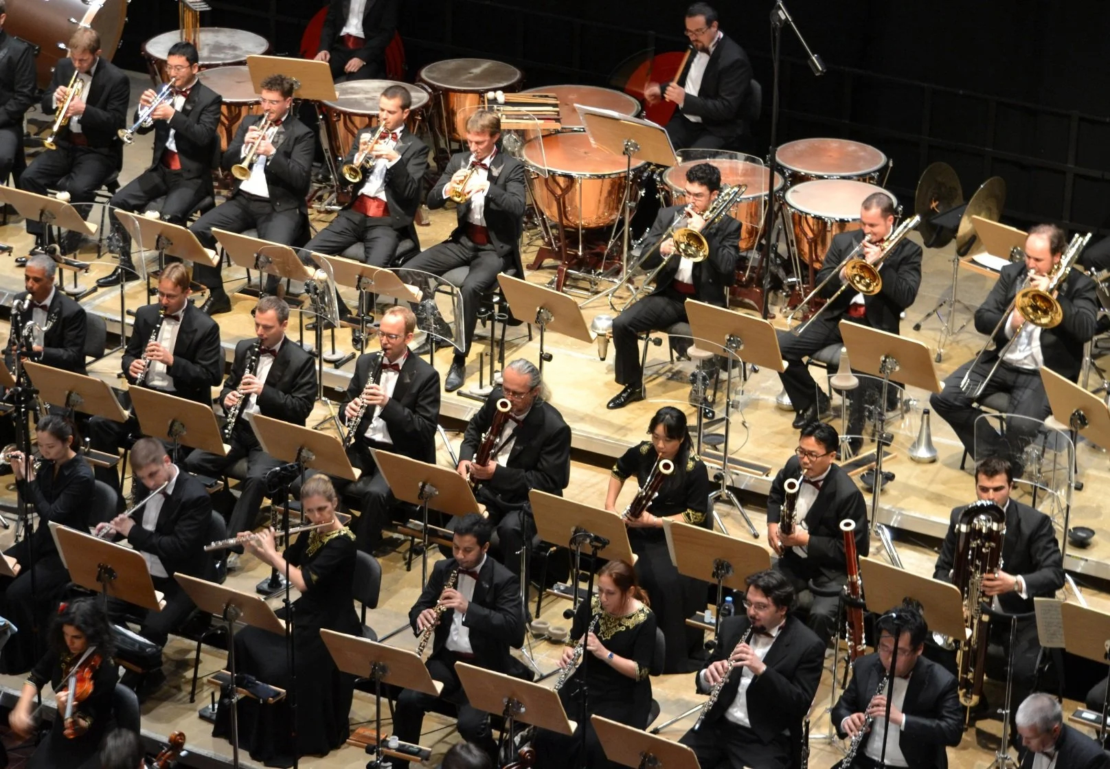 Ein Orchester während eines Auftritts im Konzertsaal, bestehend aus Musikern mit verschiedenen Instrumenten, die auf einer Bühne sitzen.