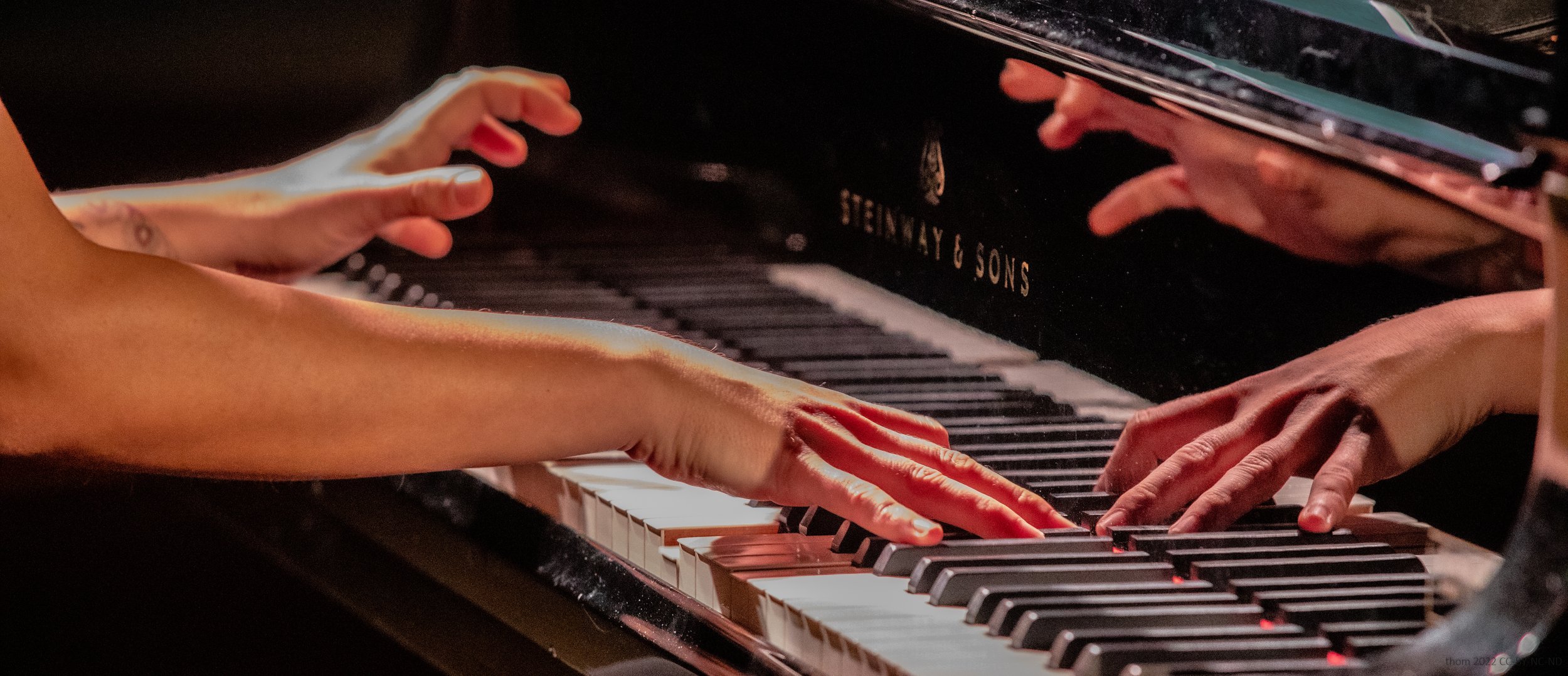 Nahaufnahme von zwei Händen, die auf den Tasten eines Klaviers spielen, mit dem Blick auf die Tastatur und das Markenzeichen 'Steinway & Sons'.
