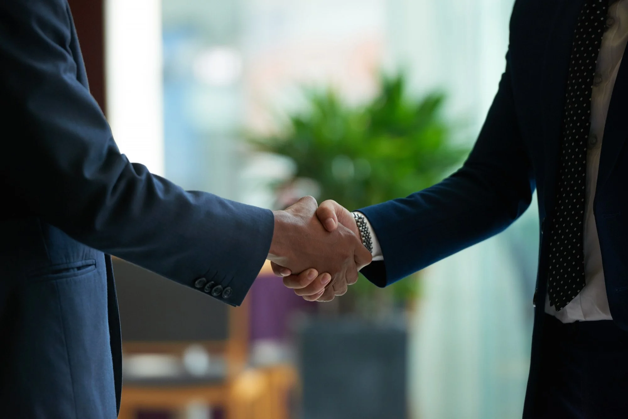 Two people in business suits shaking hands in an office setting.