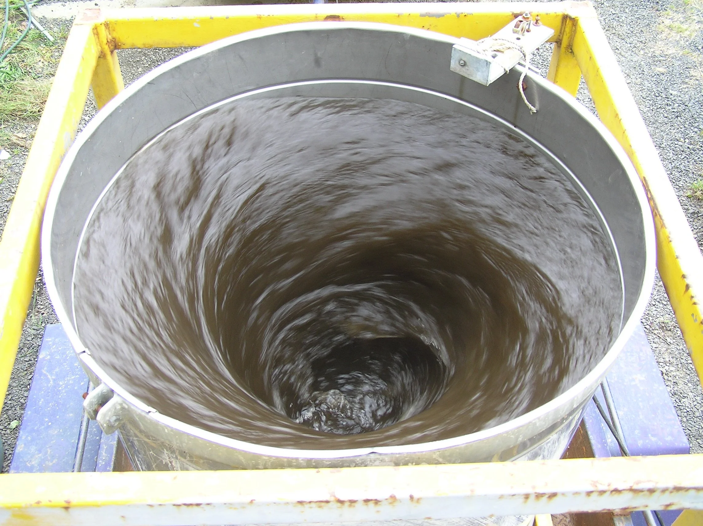 A large metal circular container with water swirling inside, mounted within a yellow metal frame.