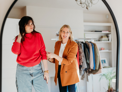Two women, one young and one older, happily chatting in a clothing store or boutique.
