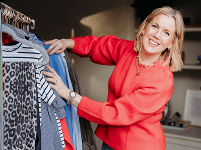 A woman smiling and shopping for clothes, holding a hanger with a garment on it.