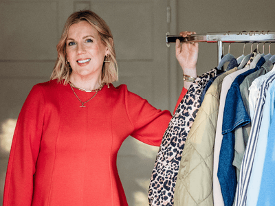 A woman in a red dress smiling while holding a clothing rack with various shirts and jackets.