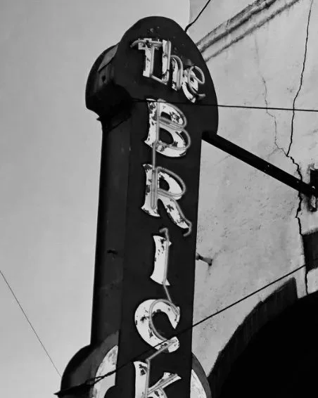 Close-up of an old, weathered vertical sign that reads "The Bakery" with some letters partially missing or damaged.