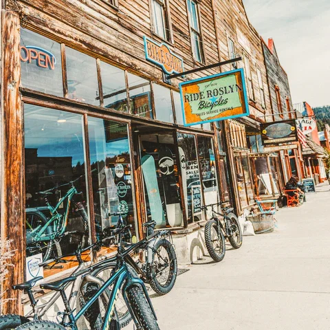 Exterior view of a bicycle shop called 'Ride Roslyn Bicycles' with bicycles displayed outside and signs indicating it is open and provides bicycle sales and service.