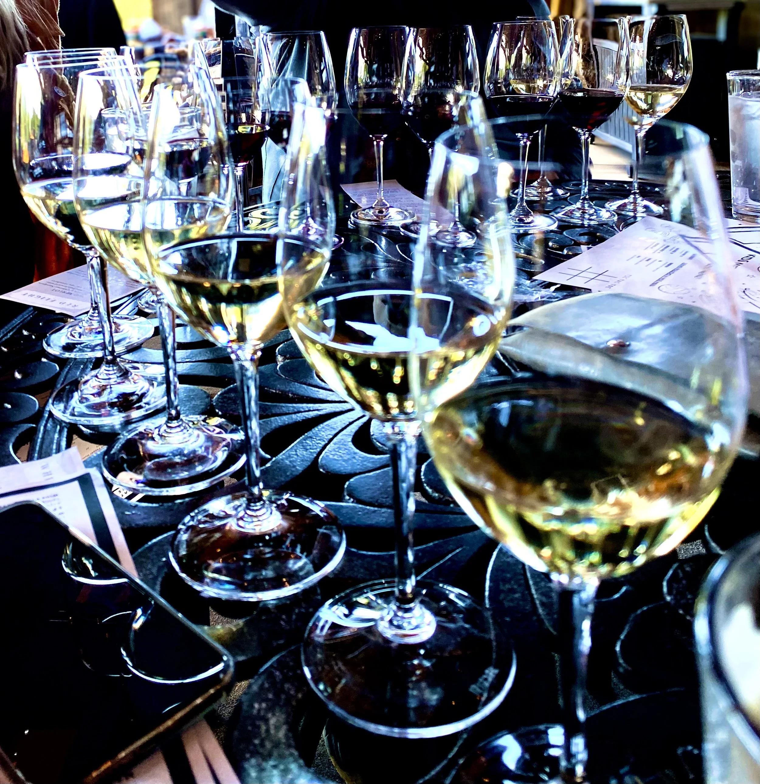 Multiple wine glasses filled with white and red wines on a black textured table at a restaurant or bar setting.