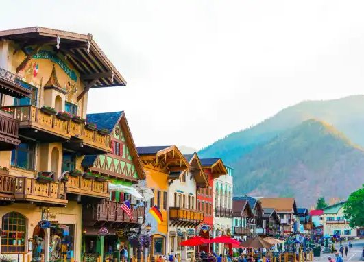 Colorful European-style buildings with outdoor cafes and shops, green mountains in the background