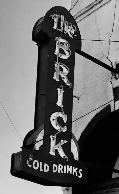 An old vertical sign that reads "The Black" at the top and "Old Drinks" at the bottom, with worn-out letters, mounted on a building wall.