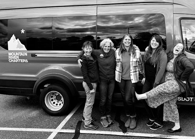 Five women standing together in front of a Mountain River Charters van, smiling and posing for a group photo outdoors.