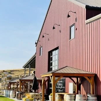 Pink building with black exterior lights, windows, and a wooden porch with barrels and outdoor seating. Yakima Winery. Winery tour