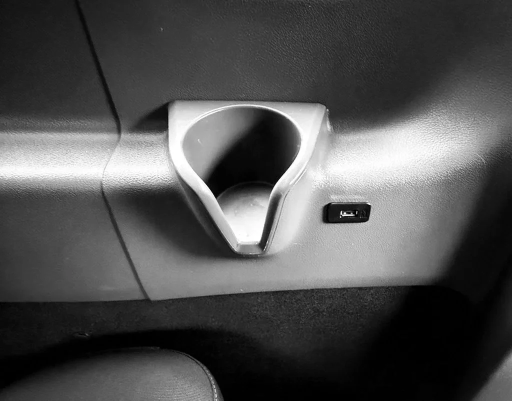 A close-up of a small automotive cup holder with a USB port nearby, embedded in a car's interior panel.