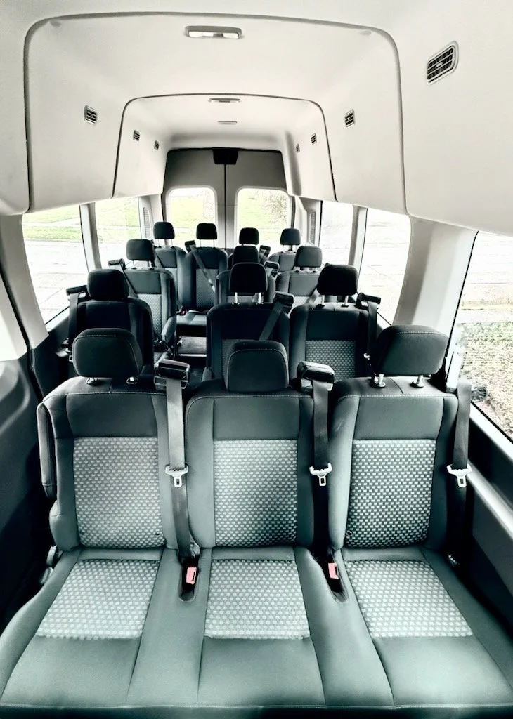 Interior of a passenger van showing three rows of black and gray fabric seats with seat belts.