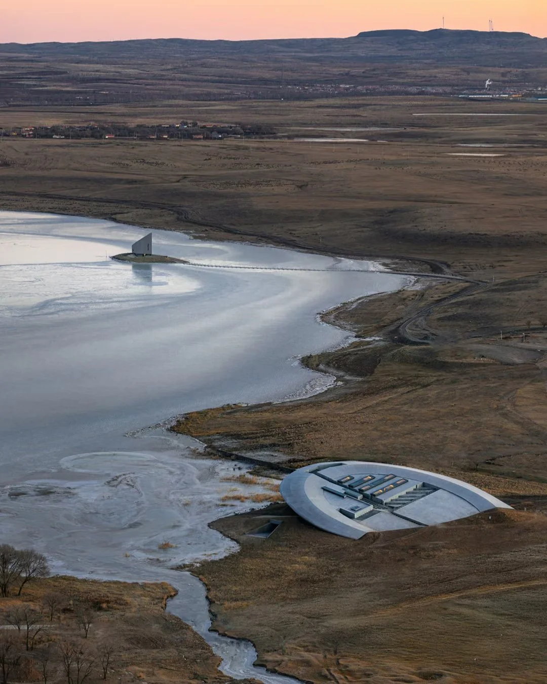Prairie Ark and Nomads' Beacon Tower sit on the flat shores of Laoli Lake in the Ulanqab Grassland of Inner Mongolia, 160km west of Beijing. Completed in 2025 by Beijing studio BUZZ, founder Ziyu Zhuang was direct about rejecting superficial cultural