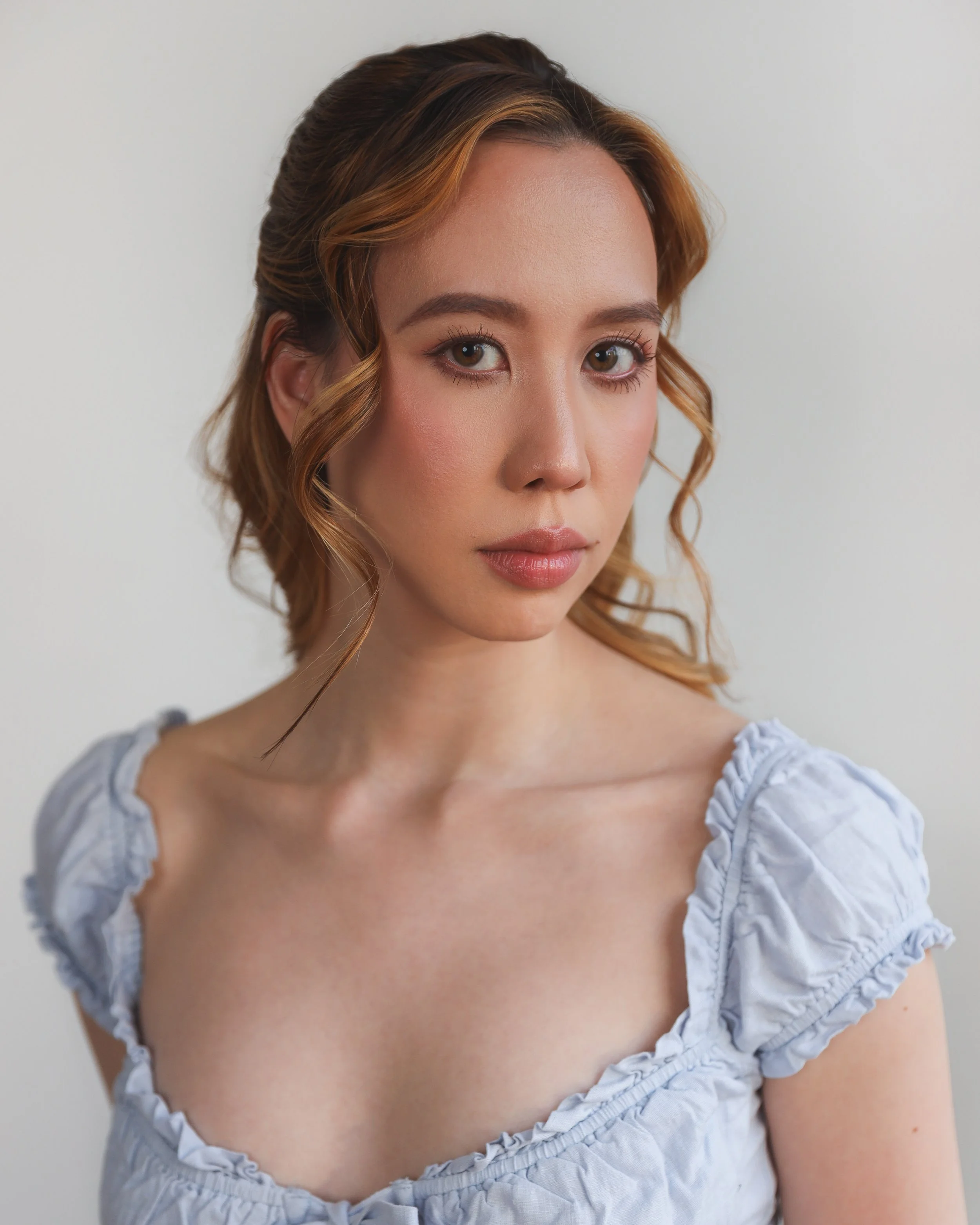 A young woman with red hair and light skin, wearing a light gray blouse with ruffled sleeves, looking at the camera against a plain white background.