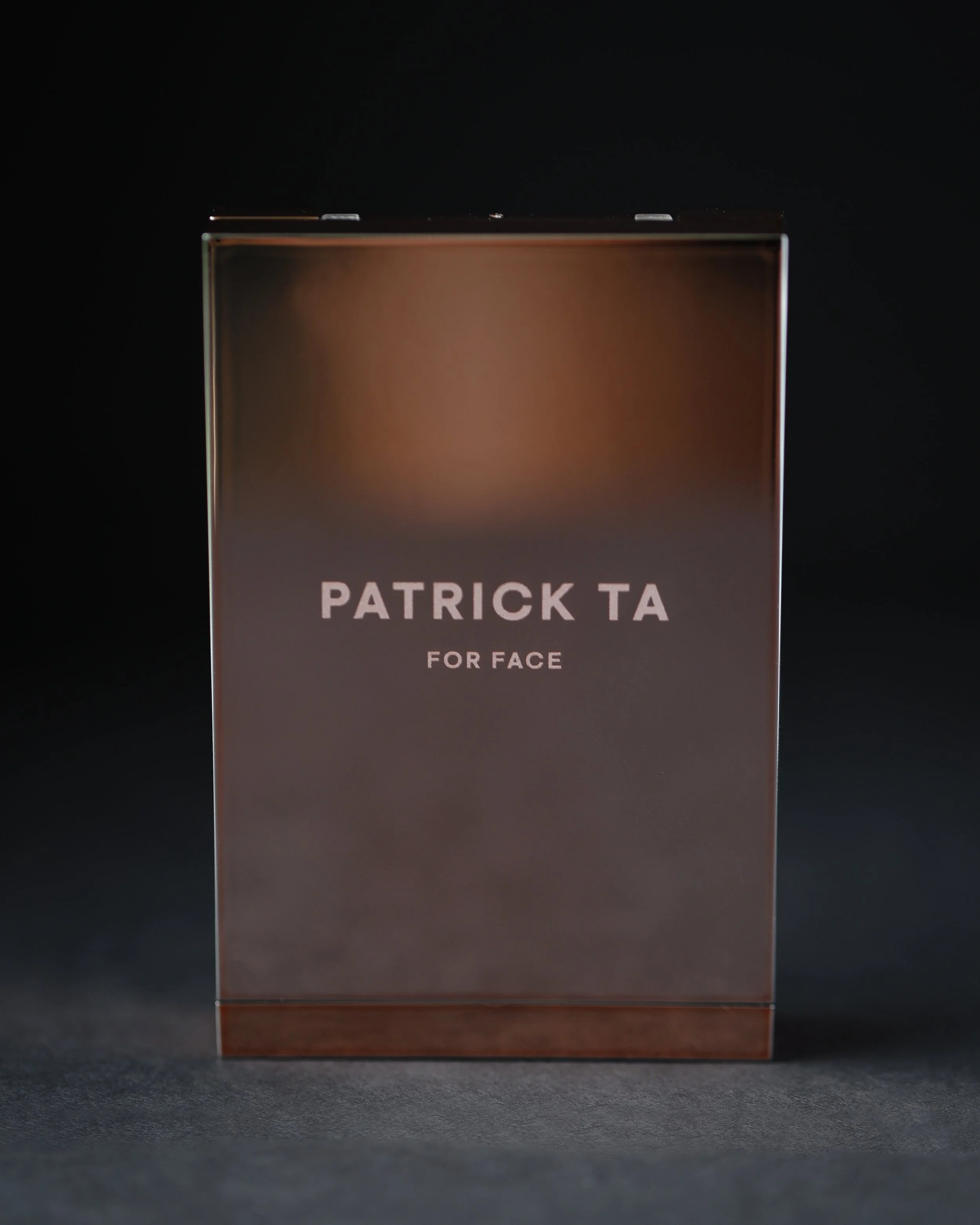 A metallic box with the text 'Patrick Ta for Face' on the front, standing against a dark background.