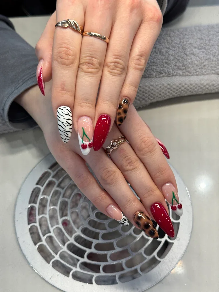 Nageldesign mit Gepardmuster, Kirschen und rotem Nagellack auf langen, spitzen Nägeln.