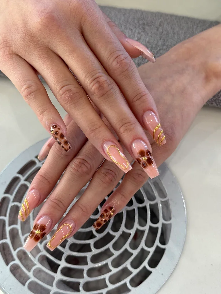 Nahaufnahme von manicürten Fingernägeln mit Leopardenmuster, goldenen Linien und klarem Nagellack.